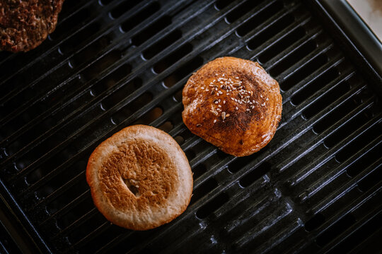Valmiera, Latvia- July 29, 2023 - Burger buns are toasted on a grill with visible grill marks and glowing coals beneath them.