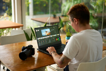 Pro videographer edits wildlife footage on laptop in a bright office. Color grading process by...