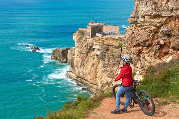 nice senior woman riding her electric mountain bike on the rocky cliffs of Nazare at the western...