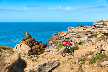 Brave senior woman riding her electric mountain bike on the rocky cliffs of Peniche at the western atlantic coast of Portugal - 789462132