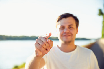 man pointing finger with positive emotion. unshaven beard young adult man shows his finger at camera on lake on sunny day. Believe in yourself concept - obrazy, fototapety, plakaty
