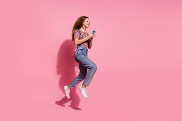 Full length photo of lovely teen lady jump hold device dressed stylish print clothes isolated on pink color background
