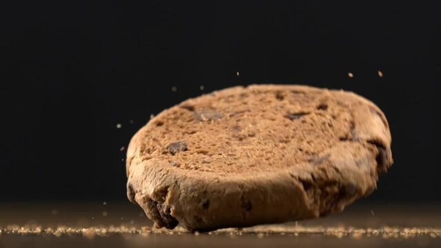 Chocolate chip cookie falls into table surface in slow-motion with crumbs flying in the air, macro close-up shot
