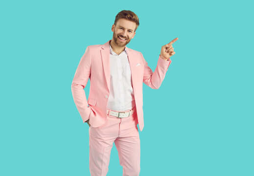 Happy man pointing to side. Handsome young man in pink suit standing with hand in pocket isolated on blue background, showing something, advertising fashion sale, smiling and pointing his finger away