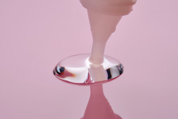 A drop of cosmetic product pours from a tube onto a pink background.