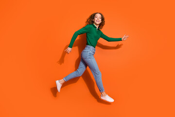 Full length photo of positive cheerful lady dressed green shirt jumping running fast emtpy space isolated orange color background