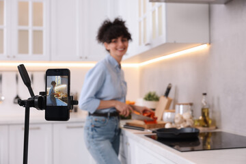 Fototapeta na wymiar Food blogger cooking while recording video in kitchen, focus on smartphone