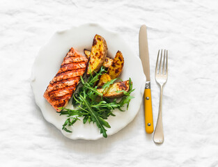 Delicious lunch - grilled salmon, baked potatoes and arugula salad on a light background, top view - 789473302