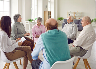 Friendly young nurse, caregiver or psychologist woman having conversation with a group of senior...
