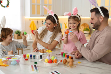 Easter celebration. Happy family with bunny ears having fun while painting eggs at white marble table in kitchen