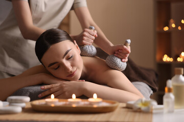 Fototapeta na wymiar Spa therapy. Beautiful young woman lying on table during herbal bag massage in salon