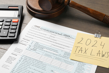 2024 tax laws. Form, paper note, calculator and gavel on wooden table, closeup