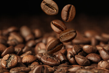 Roasted coffee beans falling on heap against dark background, closeup