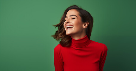Fototapeta premium A vibrant image capturing a woman in a red turtleneck, eyes closed in a moment of genuine laughter, exuding warmth and happiness against a green background.