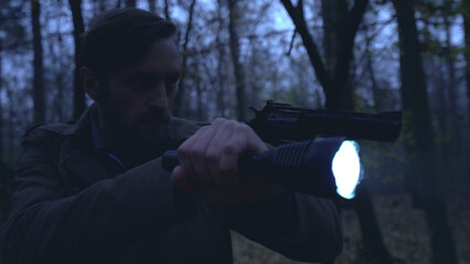 Detective chases the murderer in a night forest, aiming his gun and shining a flashlight 
