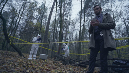 Forensic experts working with evidence in a forest, detective taking notes about the crime scene 