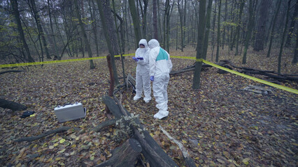 Forensic scientist examining a hazardous part of the forest wearing protective suits, assessing...