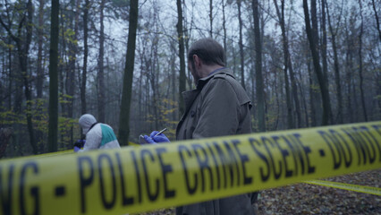 Detective surveys the crime scene and makes notes, cataloging evidence 