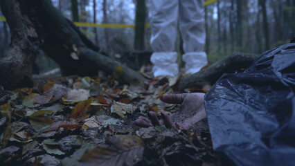 Criminalist photographs the hand of a deceased female found hidden in the forest, conducting an...