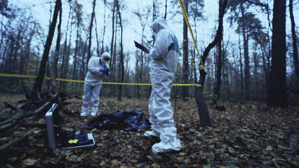Investigators in protective uniforms collect evidence at a forest crime scene 
