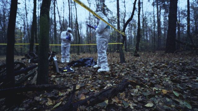 Experts in protective gear examine a murder scene in the forest, applying forensic science 
