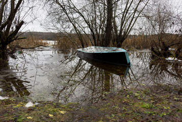 A sunken boat in the river in the spring flooding. A fishing boat is sunk in the lake. Spring flood on the lake shore. High water level in the lake. The river overflowed its banks