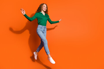 Full length photo of excited girly lady dressed green shirt jumping high walking emtpy space isolated orange color background