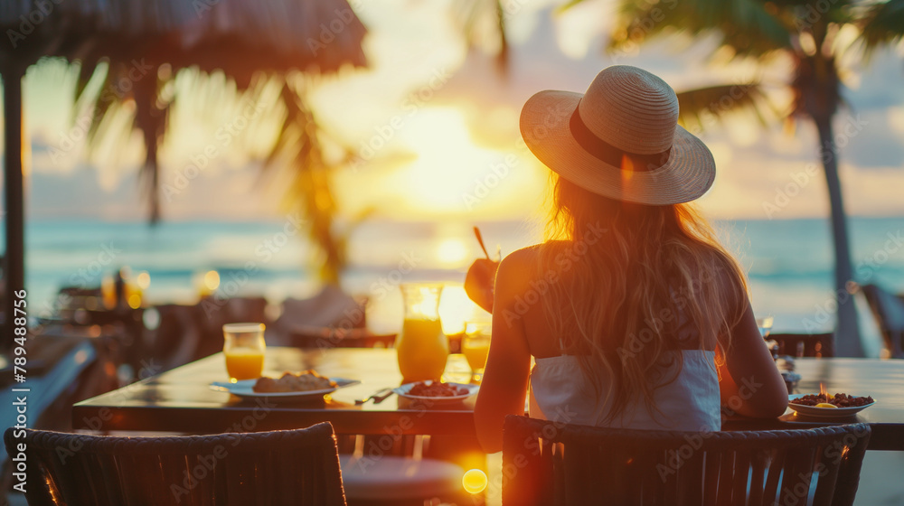 Wall mural female tourist enjoying sunset dinner by the beach: tropical vacation