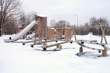 Wooden playground made of natural eco-friendly material in public city park with snow at winter time. Modern safety children outdoor equipment. Winter activities. Children rest and games on open air