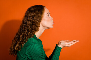 Photo of flirty dreamy lady dressed green shirt blowing arms kiss emtpy space isolated orange color background