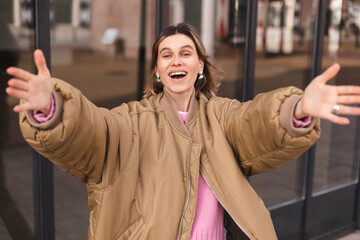 Beautiful brunette young woman wear bomber jacket looking at the camera smiling with open arms for...