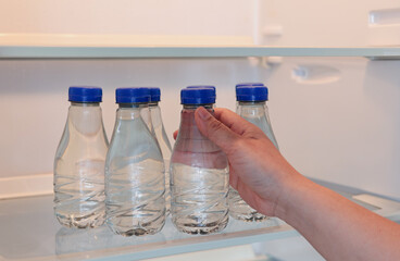 A hand taking out a water bottle or mineral water from refrigerator or a fridge. Drinking water is beneficial to health.