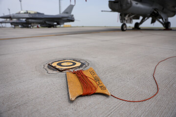 Electrical grounding cables are seen on a runway. Military fighter aircraft in the background. - 789495384