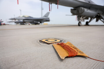 Electrical grounding cables are seen on a runway. Military fighter aircraft in the background. - 789495395