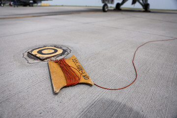 Electrical grounding cables are seen on a runway. Military fighter aircraft in the background. - 789495397
