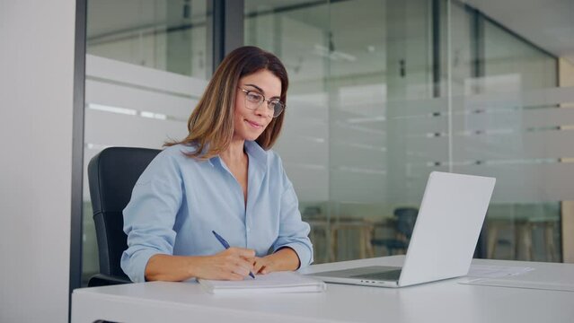 Mature business woman manager having hybrid office meeting. Busy middle aged female executive conducting online interview by video digital conference call, watching webinar looking on laptop at work.
