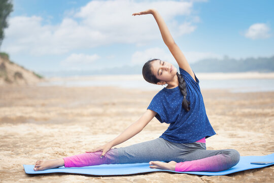 athlete indian women doing Parivrtta Janu Sirsasana pose stretching yoga at a sea beach on a yoga mat
