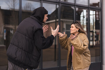 Young arguing sad couple two friends family man woman in casual clothes screaming scolding together walking outdoor near glass office. Man yelling at woman. Couple arguing, having relationship problem