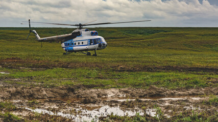 An Mi-8 passenger helicopter made an emergency landing in the northern summer tundra. Beautiful cloudy sky on the horizon. Green grass - obrazy, fototapety, plakaty