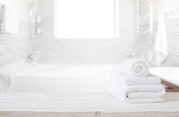 White towels on wooden table top with copy space on blurred bathroom background - obrazy, fototapety, plakaty