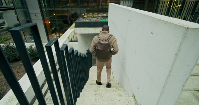 A man in a sweater, with a briefcase on his shoulders, goes down the city stairs outdoors, rear view, unrecognizable person