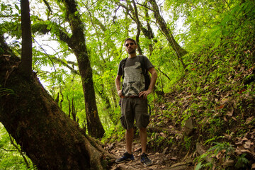 View of a young man wearing sunglasses hiking along the forest path. 
