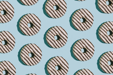 Glazed chocolate donuts pattern on pastel blue background, creative sweet food wallpaper.