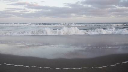 Panorama view of the ocean waves and beach under a sunset sky. The landscape reflection in the...