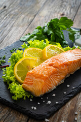 Smoked salmon with lemon and greens on black stony plate on wooden background
