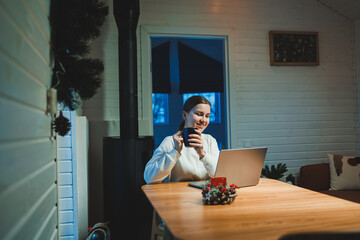 Smiling happy woman working on laptop while sitting at table. Young creative woman working and typing on keyboard at home. Work at home concept - obrazy, fototapety, plakaty