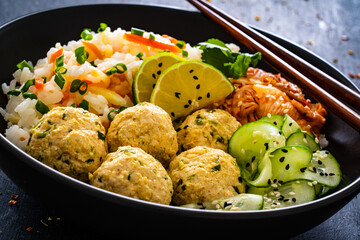 Meatballs served with white rice and marinated sliced cucumber on wooden background
