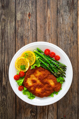 Crispy breaded fried pork chop, green asparagus and fresh vegetables on wooden table
