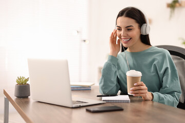 Young woman in headphones watching webinar at table in room
