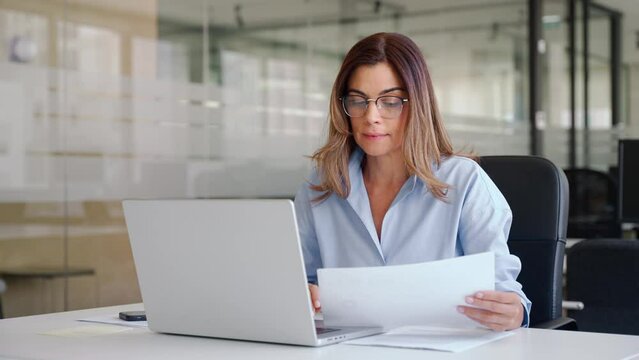 Busy 40 years old business woman entrepreneur working in office checking documents in office. Businesswoman of middle age account manager executive or lawyer using laptop computer at work.
